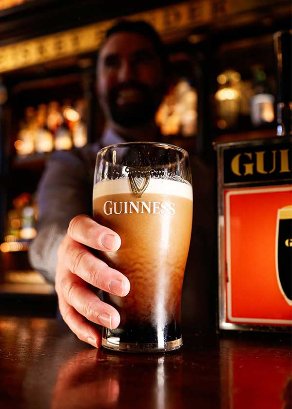 A barman presents a pint of Guinness to the viewer